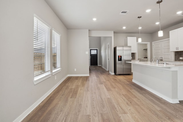 18737 Bliss Pl, New Caney, TX 77357 - kitchen with stainless steel fridge, light countertops, light wood finished floors, white cabinetry, and pendant lighting