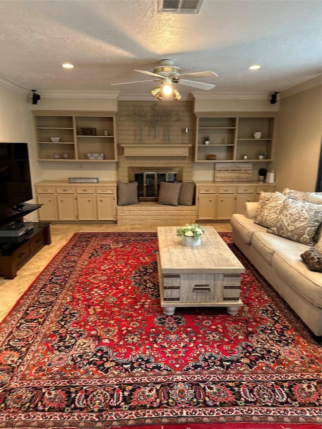 living area with ornamental molding, ceiling fan, a textured ceiling, and a fireplace