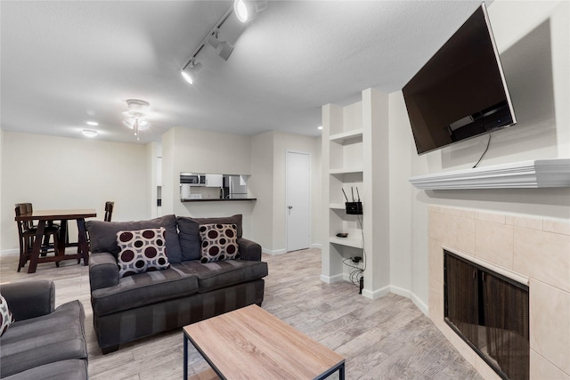 2601 S Braeswood Blvd S Unit 1403, Houston, TX 77025 - living room featuring a tile fireplace, light wood-style flooring, built in features, a ceiling fan, and baseboards