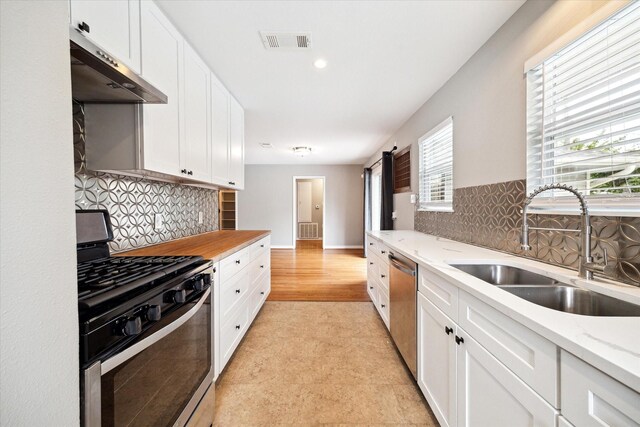 2009 Sedgie Dr, Houston, TX 77080 - kitchen featuring appliances with stainless steel finishes, a sink, under cabinet range hood, white cabinetry, and decorative backsplash