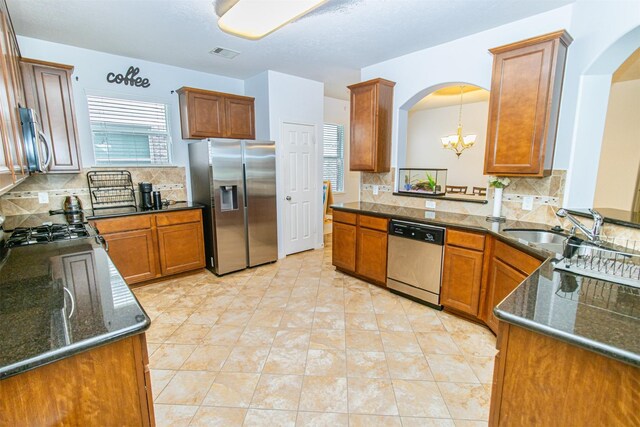 15102 Dry Ridge Ct, Humble, TX 77346 - kitchen with stainless steel appliances, arched walkways, brown cabinetry, a sink, and a chandelier
