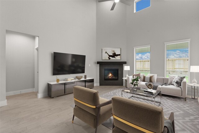 231 Upland Dr, Waller, TX 77484 - living room with a towering ceiling, a ceiling fan, a glass covered fireplace, light wood-style flooring, and baseboards