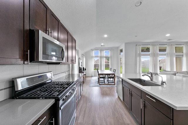25219 Easton Ramsey Way, Richmond, TX 77406 - kitchen featuring stainless steel appliances, a sink, light wood finished floors, dark brown cabinetry, and a center island with sink