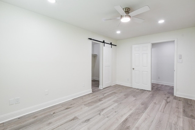 527 Fm 787th Rd E, Cleveland, TX 77327 - unfurnished bedroom with a barn door, light wood-style floors, a walk in closet, recessed lighting, and baseboards