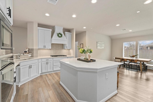 2221 Hay Field Ct, Conroe, TX 77384 - kitchen with custom range hood, appliances with stainless steel finishes, light wood-type flooring, a kitchen island, and recessed lighting