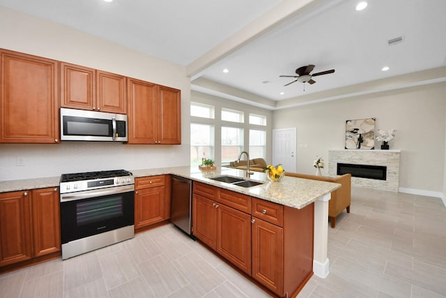 2003 Marthoman Dr, Missouri City, TX 77489 - kitchen with appliances with stainless steel finishes, a sink, a peninsula, a glass covered fireplace, and brown cabinets