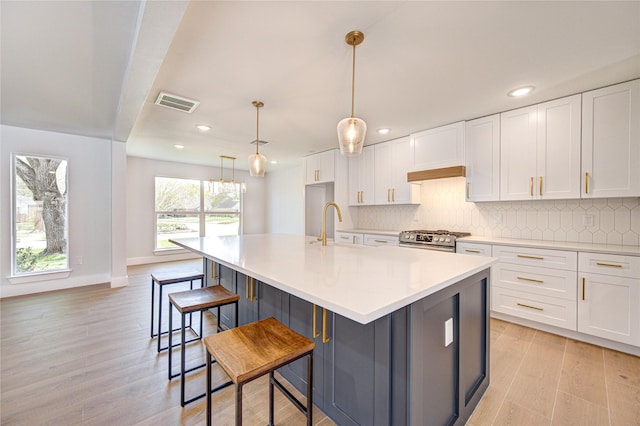 1810 Eagle Falls Ct, Houston, TX 77077 - kitchen with stainless steel range with gas cooktop, light wood-type flooring, decorative backsplash, white cabinets, and an island with sink