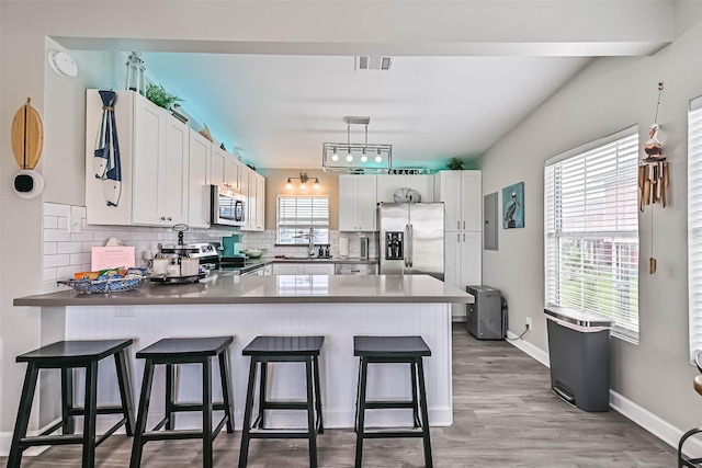 4126 Reeves Dr, Galveston, TX 77554 - kitchen featuring appliances with stainless steel finishes, a peninsula, white cabinets, and tasteful backsplash