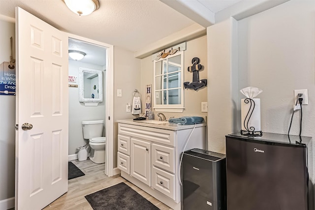 4126 Reeves Dr, Galveston, TX 77554 - bathroom with toilet, wood finished floors, vanity, a textured ceiling, and baseboards