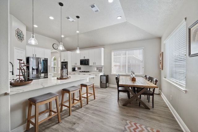 2517 Royal Terns Ct, League City, TX 77573 - kitchen with stainless steel refrigerator with ice dispenser, black microwave, lofted ceiling, a kitchen breakfast bar, and light wood-style flooring