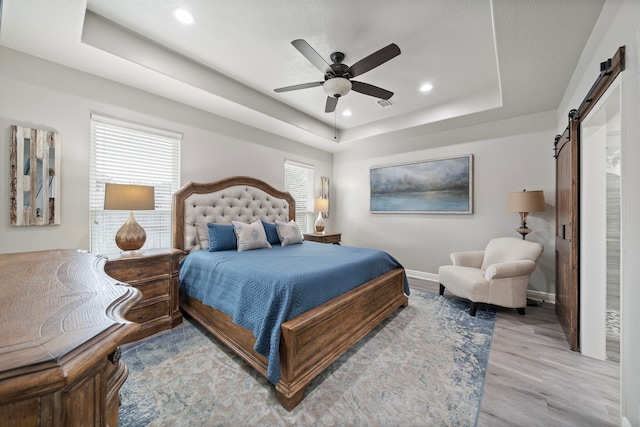 2517 Royal Terns Ct, League City, TX 77573 - bedroom featuring a barn door, a tray ceiling, light wood-style flooring, baseboards, and ceiling fan