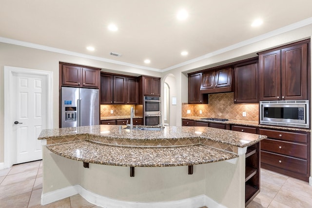 95 W Hullwood Cir, The Woodlands, TX 77389 - kitchen featuring appliances with stainless steel finishes, a spacious island, dark brown cabinetry, a kitchen breakfast bar, and dark stone countertops