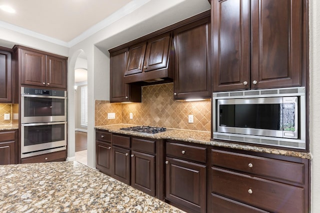 95 W Hullwood Cir, The Woodlands, TX 77389 - kitchen with appliances with stainless steel finishes, arched walkways, ornamental molding, dark brown cabinets, and light stone countertops