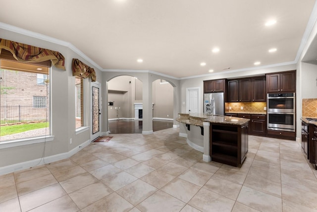 95 W Hullwood Cir, The Woodlands, TX 77389 - kitchen with stainless steel appliances, crown molding, decorative backsplash, arched walkways, and dark brown cabinetry