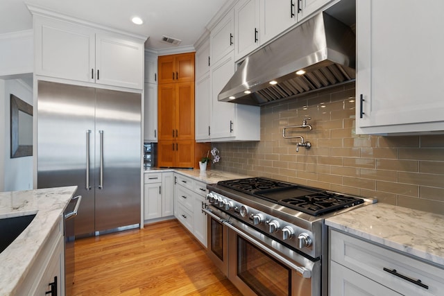 4021 Glenshire St, Houston, TX 77025 - kitchen featuring under cabinet range hood, high quality appliances, decorative backsplash, white cabinetry, and light stone counters
