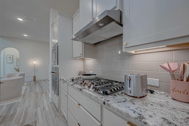 5038 Galahad Ct, Missouri City, TX 77459 - kitchen with ventilation hood, appliances with stainless steel finishes, backsplash, white cabinets, and arched walkways
