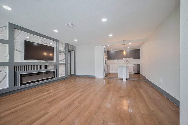 6058 Lyndhurst Dr, Houston, TX 77033 - unfurnished living room featuring light wood-type flooring, baseboards, a sink, recessed lighting, and a glass covered fireplace