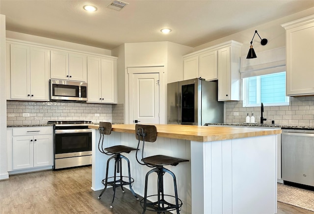 12531 Hilltop Mill Rd, Magnolia, TX 77354 - kitchen featuring appliances with stainless steel finishes, butcher block counters, tasteful backsplash, a kitchen island, and white cabinetry