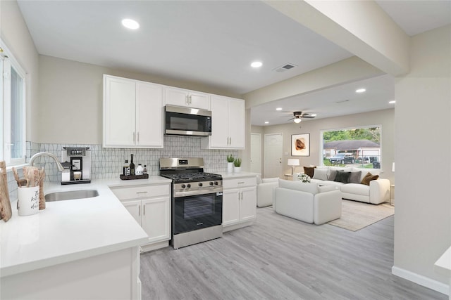 9409 Fairland Dr, Houston, TX 77051 - kitchen featuring appliances with stainless steel finishes, a sink, light wood-style flooring, backsplash, and white cabinetry