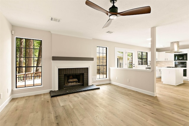 50 E Copper Sage Cir, The Woodlands, TX 77381 - unfurnished living room with light wood-style floors, a ceiling fan, baseboards, and a brick fireplace