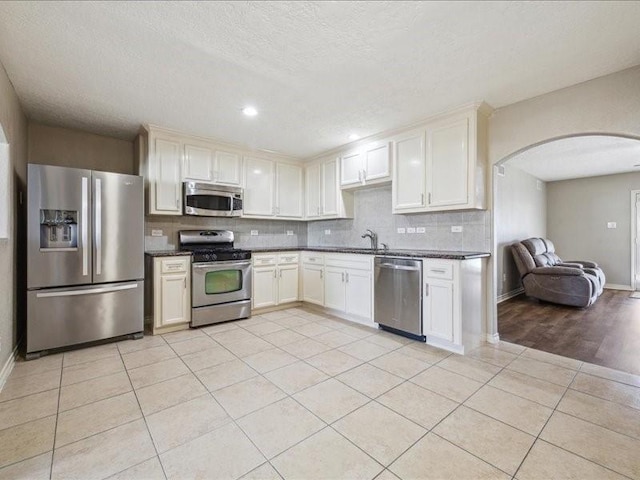 7205 Yucca Dr, Galveston, TX 77551 - kitchen with appliances with stainless steel finishes, arched walkways, dark countertops, tasteful backsplash, and light tile patterned floors
