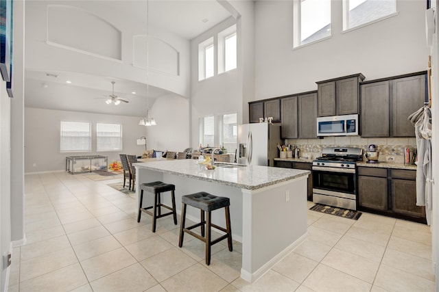 24210 Leonforte Dr, Richmond, TX 77406 - kitchen with stainless steel appliances, a high ceiling, light tile patterned flooring, a breakfast bar area, and tasteful backsplash