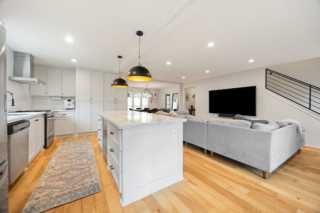 10310 Helmsdale St, Houston, TX 77043 - kitchen featuring appliances with stainless steel finishes, wall chimney range hood, light wood-style floors, a center island, and recessed lighting