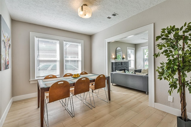 1522 Munger St, Houston, TX 77023 - dining space featuring light wood-style floors, baseboards, a fireplace, and a textured ceiling