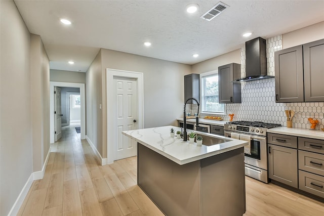 1522 Munger St, Houston, TX 77023 - kitchen with stainless steel gas range oven, wall chimney exhaust hood, gray cabinetry, a sink, and recessed lighting