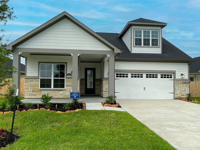 1306 Hidden Oaks Dr, Tomball, TX 77375 - view of front of home with stone siding, covered porch, concrete driveway, a front yard, and a shingled roof