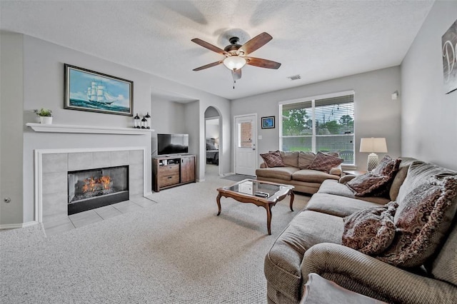 7126 Leens Lodge Ln, Humble, TX 77346 - carpeted living room with arched walkways, a tiled fireplace, ceiling fan, a textured ceiling, and baseboards