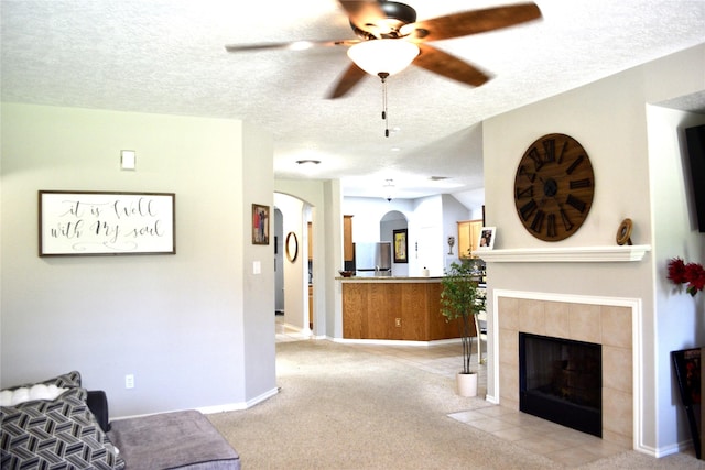 7126 Leens Lodge Ln, Humble, TX 77346 - living room featuring arched walkways, a textured ceiling, ceiling fan, a fireplace, and light colored carpet
