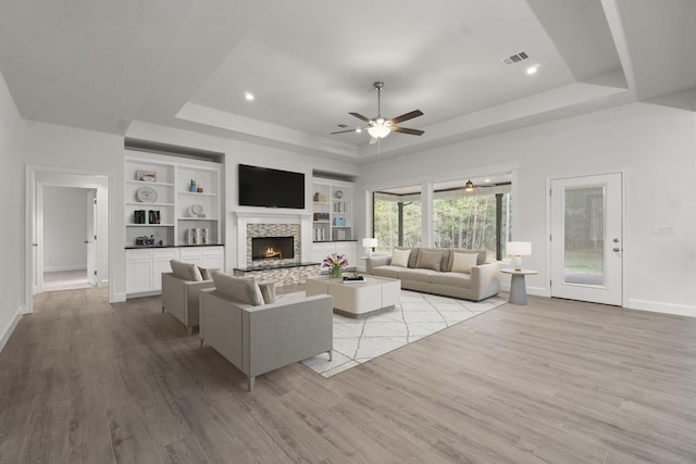 28200 E Stallion Ln, Waller, TX 77484 - living room featuring a raised ceiling, baseboards, light wood finished floors, a stone fireplace, and a ceiling fan