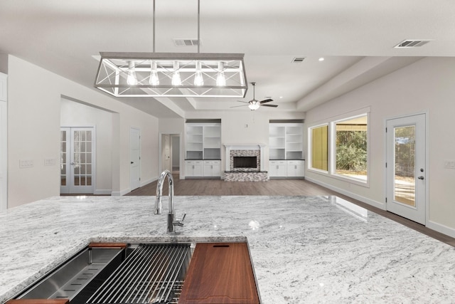 28200 E Stallion Ln, Waller, TX 77484 - kitchen featuring a stone fireplace, a ceiling fan, wood finished floors, and light stone counters
