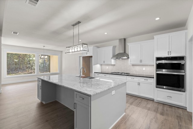 28200 E Stallion Ln, Waller, TX 77484 - kitchen featuring wall chimney exhaust hood, a sink, stainless steel appliances, light wood-style floors, and white cabinetry