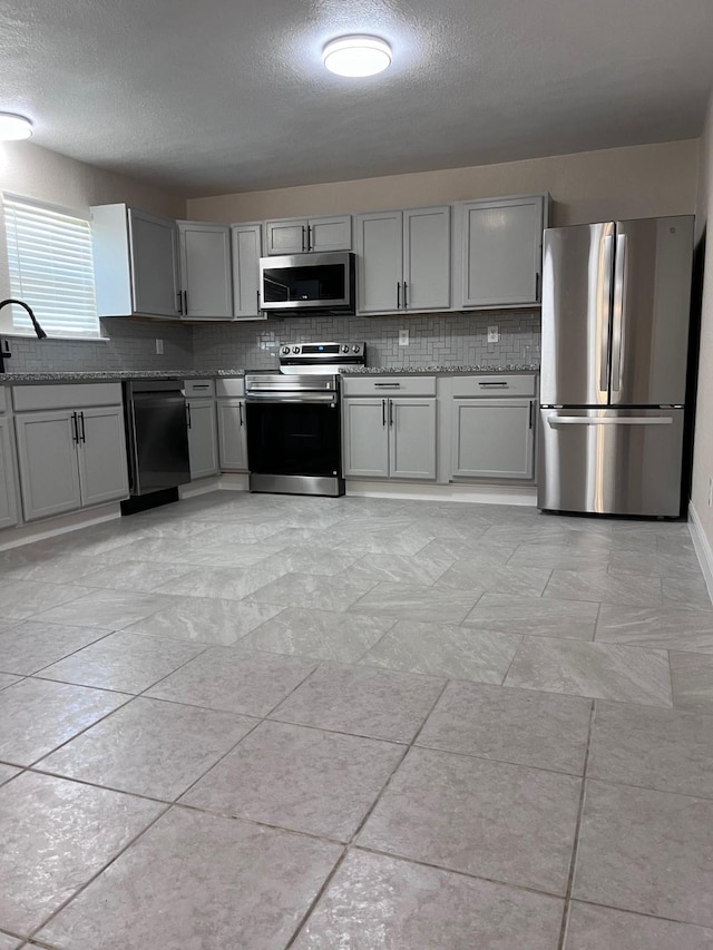 8330 Blue Quail Dr, Houston, TX 77489 - kitchen with stainless steel appliances, gray cabinetry, a sink, decorative backsplash, and a textured ceiling