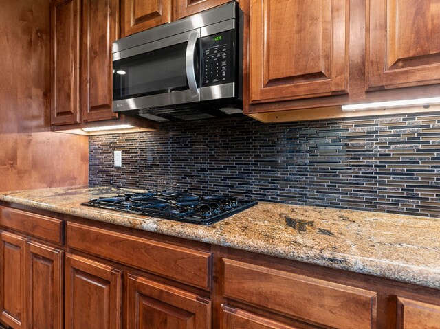14624 Dove Ln, Needville, TX 77461 - kitchen with stainless steel microwave, black gas cooktop, tasteful backsplash, and light stone countertops