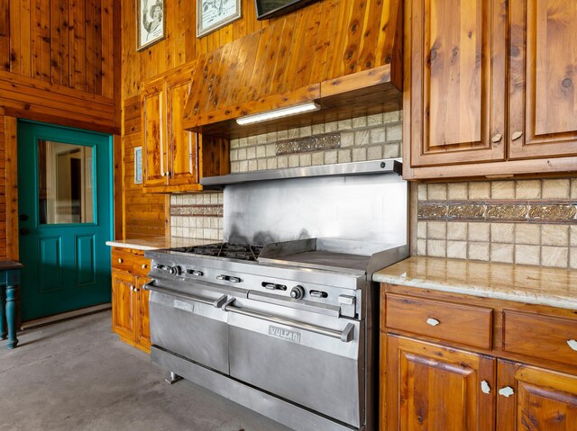 14624 Dove Ln, Needville, TX 77461 - kitchen featuring double oven range, wooden walls, concrete floors, brown cabinets, and custom exhaust hood