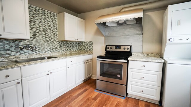 1126 Ryon St, Houston, TX 77009 - kitchen featuring stainless steel electric stove, estacked washer and dryer, a sink, light wood-style flooring, and decorative backsplash