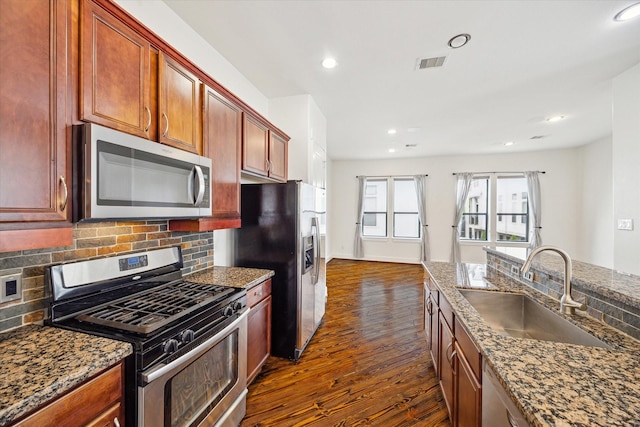 5714 Kansas St, Houston, TX 77007 - kitchen with appliances with stainless steel finishes, a sink, dark wood-style floors, decorative backsplash, and dark stone counters