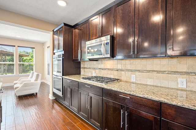 4911 Lattimore Creek Dr, Houston, TX 77084 - kitchen featuring appliances with stainless steel finishes, light stone countertops, baseboards, dark brown cabinetry, and backsplash