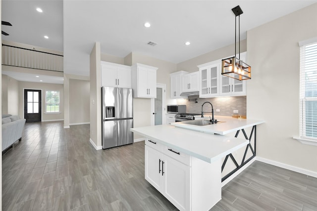 40380 Mostyn Dr, Magnolia, TX 77354 - kitchen with stainless steel appliances, a sink, a peninsula, glass insert cabinets, and light countertops
