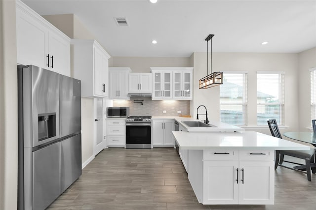 40380 Mostyn Dr, Magnolia, TX 77354 - kitchen featuring appliances with stainless steel finishes, a peninsula, a sink, light countertops, and white cabinets