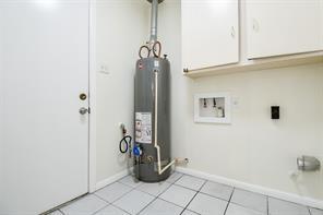 5502 Dumfries Dr, Houston, TX 77096 - laundry room with cabinet space, water heater, electric dryer hookup, baseboards, and light tile patterned flooring