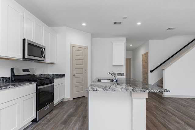407 Emma St, Angleton, TX 77515 - kitchen with stainless steel appliances, a sink, dark stone countertops, dark wood-type flooring, and a center island with sink