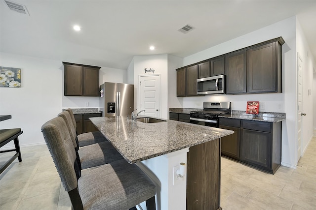1023 Cattle Chute Ct, Rosharon, TX 77583 - kitchen featuring stainless steel appliances, a sink, dark stone counters, dark brown cabinets, and a breakfast bar area