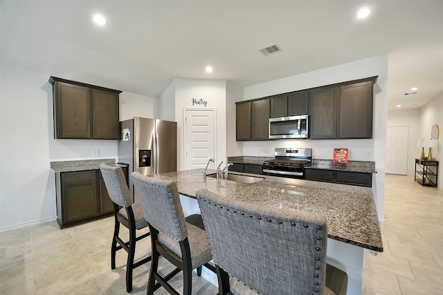 1023 Cattle Chute Ct, Rosharon, TX 77583 - kitchen featuring stainless steel appliances, dark brown cabinetry, dark stone counters, a breakfast bar, and a sink