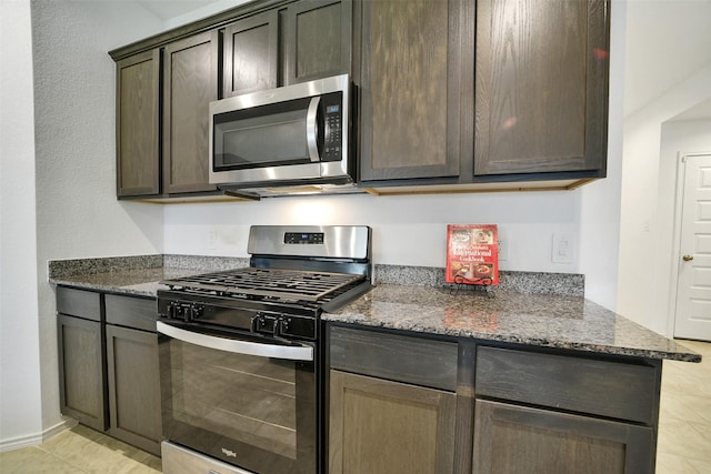 1023 Cattle Chute Ct, Rosharon, TX 77583 - kitchen featuring appliances with stainless steel finishes, dark stone counters, dark brown cabinetry, light tile patterned floors, and baseboards