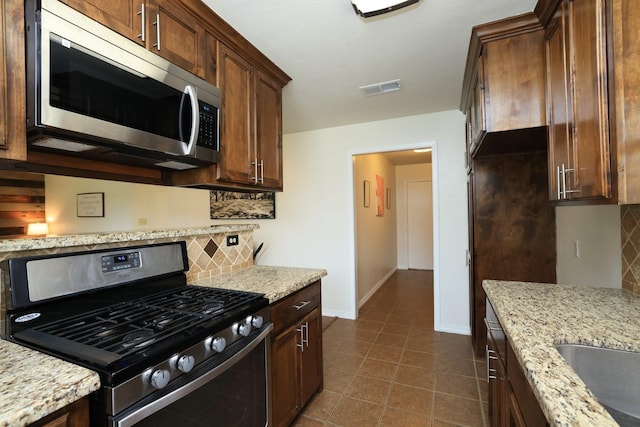 3000 Stevens Dr, Bryan, TX 77803 - kitchen with stainless steel appliances, backsplash, light stone counters, and baseboards
