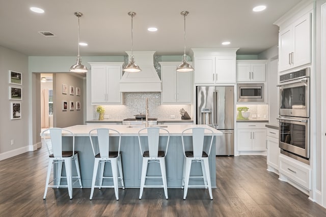 25007 Coperti Ln, Spring, TX 77386 - kitchen featuring appliances with stainless steel finishes, custom exhaust hood, a kitchen island with sink, decorative backsplash, and dark wood finished floors